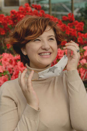 A beautiful woman removes protective face mask and inhales among spring flowersの写真素材