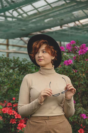 A beautiful plus size girl with eyeglasses and hat smiling among the green plants and flowers.の写真素材