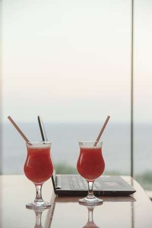 A strawberry cocktail next to a laptop in a bar overlooking the sea. Remote work on vacation concept.の写真素材