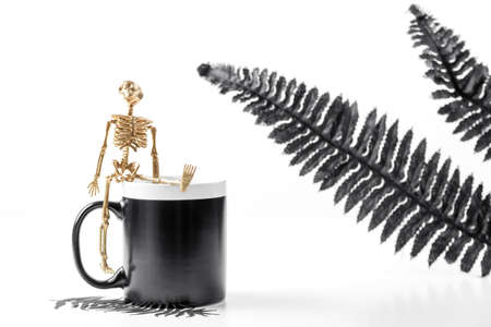 Black mug mockup. Halloween concept with stylish details golden skeleton and black leaves. Styled Stock Photography.の写真素材