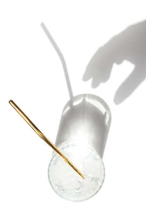 Transparent glass of water with reusable metal eco straw in sunlight with shadows and female hand.の写真素材