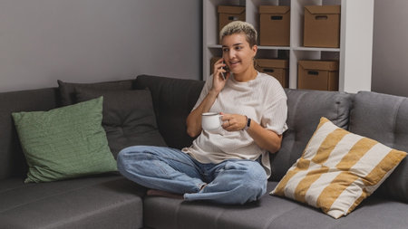 A woman lies on a sofa with a smartphone in a minimalistic home interior.