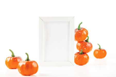 Mockup for autumn invitation card or design in white frame next to orange small pumpkins on a white background.の写真素材