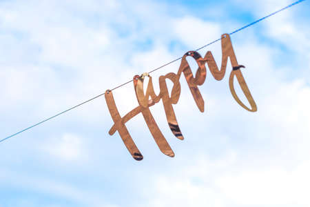 Golden word happy hangs on garland against background of blue sky with clouds. Concept of celebration of life, happiness and mental health.の写真素材