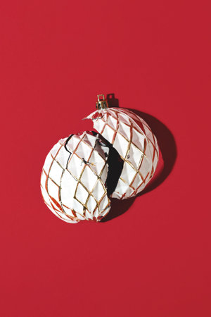White Christmas ball with shattered or broken shell on red background. Minimalistic creative trendy Christmas composition.の写真素材