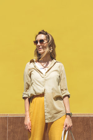 Stylish woman in yellow outfit against bright color wallの写真素材