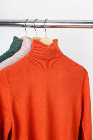 Blank turtleneck sweater mockup on clothes hanger. Bright orange ocher roll-neck with beige and green. Mock up on plain in minimal interior.の写真素材