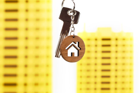 Real estate concept. Keys with house shaped keychain against bright yellow house models.