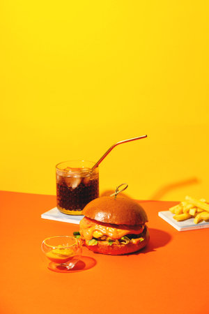 Big burger with french fries and sauce on bright orange and yellow background. American Fast food cuisine.の写真素材