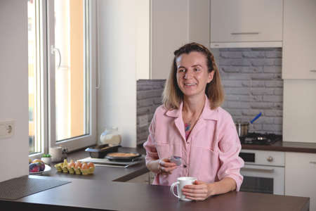 Authentic woman portrait with macaron and cup on tea in hands on her cozy home kinchen.の写真素材