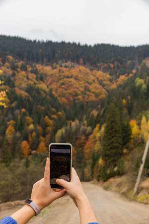 Woman taking photo on her smartphone of mountain and autumn forest. Fall colors.の写真素材