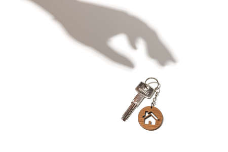 Real estate concept. Keys with house shaped keychain with hand shadow on white background.の写真素材