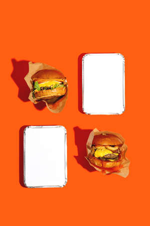 Two big burgers with cheese in a package on a bright orange background. Fast food delivery. Top view.の写真素材