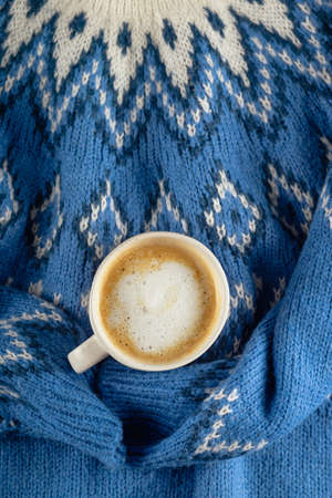 Blue sweater holding white minimalistic cup of coffee with milk. Nobody flat lay.の写真素材