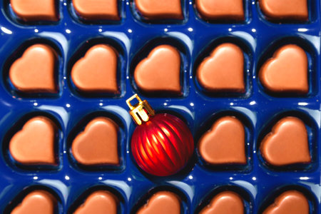 Creative Christmas concept with Christmas ball in box of heart shaped chocolates. Top view.