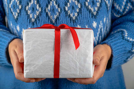 Woman in blue sweater holding white minimalistic christmas giftの写真素材