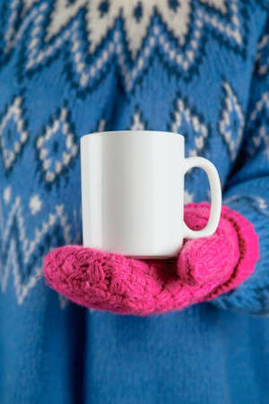 Christmas white mug mock up in hand on woman wearing pink mittens and blue sweater.の写真素材