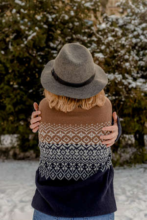 Blonde young woman in gray hat and sweater stands with her back. Background of christmas trees in snow. Winter season.の写真素材