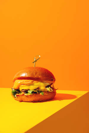Big burger with cheese on bright orange and yellow background. American Fast food cuisine in a modern style.の写真素材