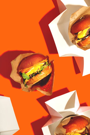 Big burger with cheese in a package on a bright orange background. Fast food delivery.の写真素材