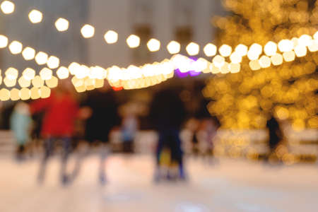 People ride skating rink on background of christmas tree in light garland. Blurred image. Wallpaperの写真素材