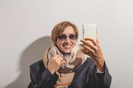 Beautiful baby boomer woman of middle age in sunglasses takes selfie on smartphone in sunlight.の写真素材