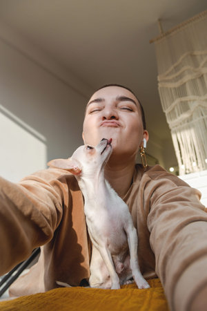 A woman with extremely short hair hugs a small chihuahua dog. Home life concept.