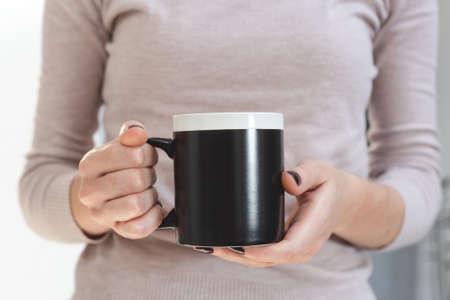 Black coffee mug mockup for design demonstration. Stylish cup mock up in female hands.の写真素材