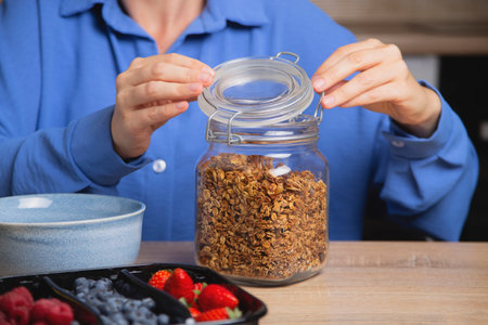 Granola in glass jar. Woman prepares quick breakfast.の写真素材