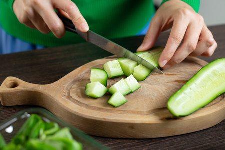 Woman cuts cucumber for cooking vegetable salad. Home kitchen.の写真素材