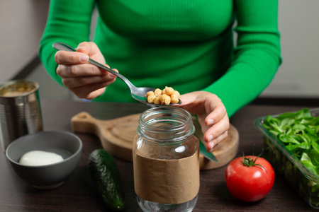 Woman making salad in jar with chickpea. Cooking healthy vegan food.の写真素材