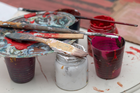 Multicolored Cans of Gouache Paint with Paintbrushes Stand on a Tableの写真素材