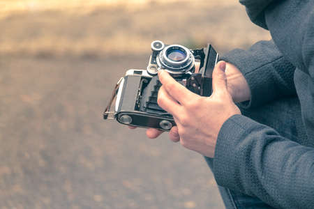 A man holds an antique, but working camera and adjusts it for photography on the streetの写真素材