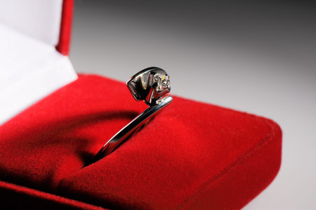 Silver finger ring with precious stone in red box over blurry gray background, selective focus