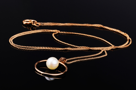 Golden chain with pendant on black mirrored surfaceの写真素材