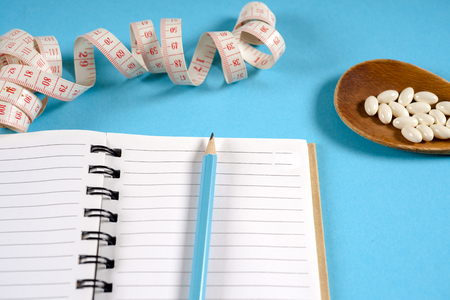 Sheet of Diet Plan and wooden spoon with a measuring tape on a blue background, diet, healthy lifestyle.の写真素材