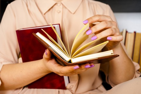 Young girl in a light dress is reading a book. Female hands hold a book in their handsの写真素材
