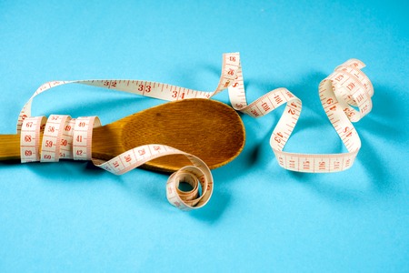 Wooden spoon with a measuring tape on a blue background, diet, healthy lifestyle.の写真素材