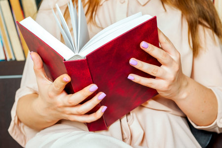 Young girl in a light dress is reading a book. Female hands hold a book in their hands