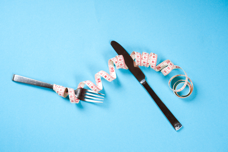 fork and knife with a centimeter on a blue background, diet, healthy lifestyle.の写真素材