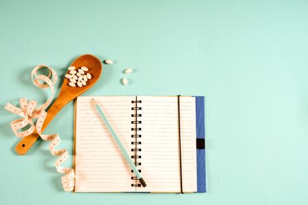 Sheet of Diet Plan and wooden spoon with a measuring tape on a blue background, diet, healthy lifestyle.の写真素材