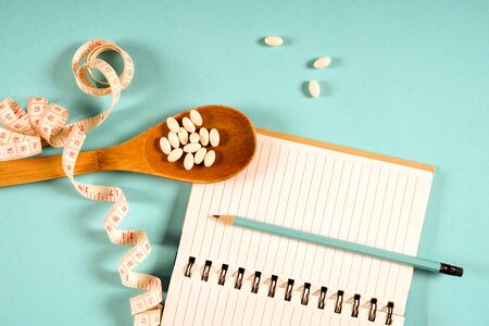 Sheet of Diet Plan and wooden spoon with a measuring tape on a blue background, diet, healthy lifestyle.の写真素材