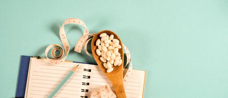 Sheet of Diet Plan and wooden spoon with a measuring tape on a blue background, diet, healthy lifestyle.の写真素材
