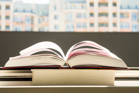 stack of books, pen oin the window with city view with top one opened and pages forming heart shape.