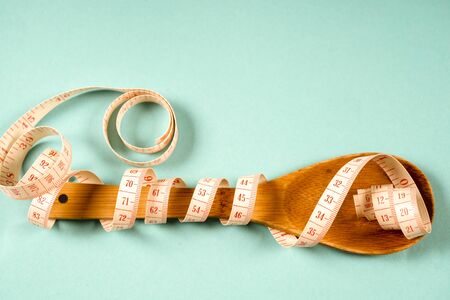 Wooden spoon with a measuring tape on a blue background, diet, healthy lifestyleの写真素材