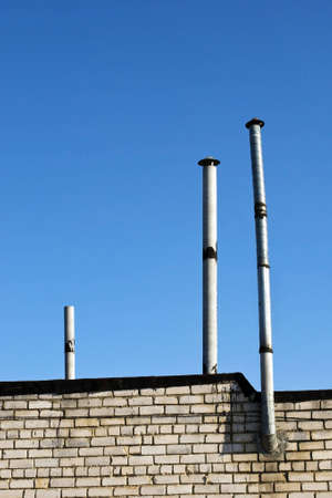 Three thin pipes, wall from a white brick and the blue skyの写真素材