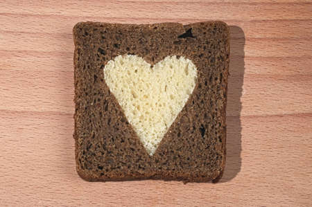 Piece of brown bread with the cut out heart from a white loaf on a chopping boardの写真素材