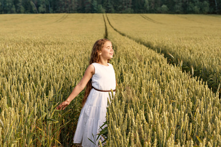 Girl enjoying the sun with arms outstretched with her eyes closed at the field of wheatの写真素材
