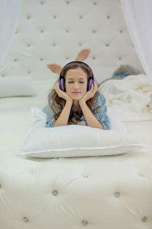 girl listening to headphones lying on a white bed with bunny ears made with feetの写真素材