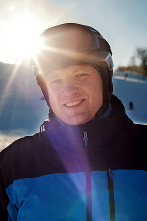 close up portrait of a man in a ski helmet and ski goggles in the sunbeams on a mountain backgroundの写真素材
